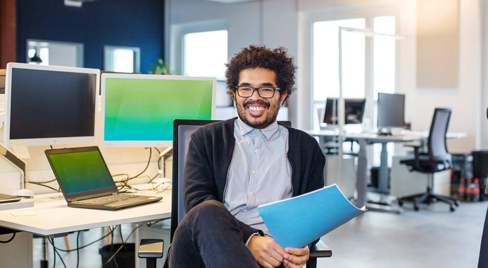 Young man holding a blue folder sitting in a modern office